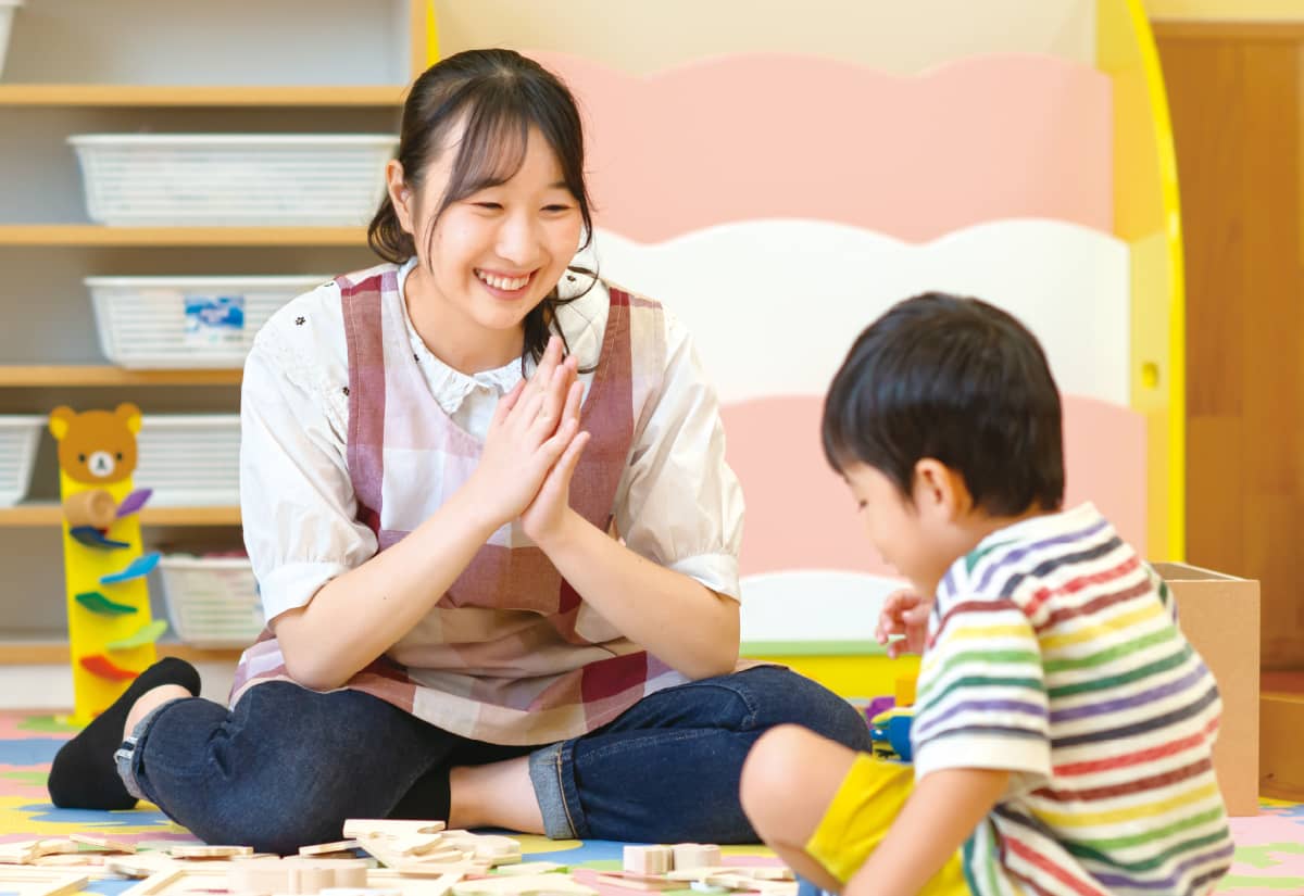 保育士の女性が子どもに対してにこやかに話しかけている